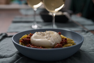 Pesto conchiglie with sundried tomatoes and burrata cheese served in blue bowl
