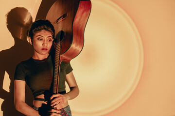 young multiracial model posing with a colorful background holding a guitar in our hand not low...