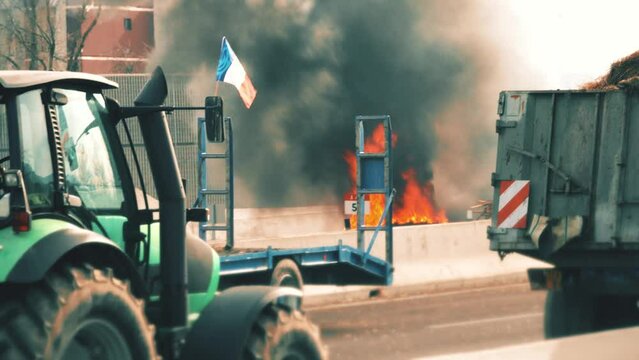 Protest of the French farmers. Burning tyres on blocked highway behind a tractor with flag of France
