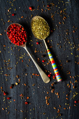 Old metal spoons with oregano and red peppercorn on black background