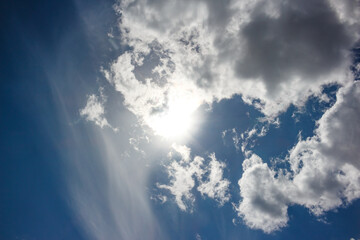 White clouds floating across the blue sky against the background of the sun