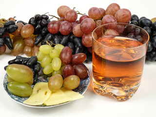Plate with cheese and grapes, drinking glass with grape juice stand on the table against a background of bunches of grapes. Appetizers and dessert.    