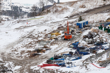 Construction site in the Altai mountains with an excavator and building materials, in the winter season at a ski resort.