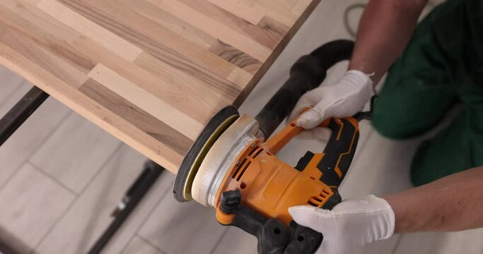 Carpenter sanding wood with sandpaper in carpentry or workshop. Electric grinder works in carpentry