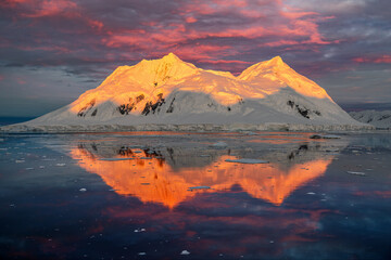 Mountain with red orange top light up by midnight sun with reflection in the sea in Antarctica 