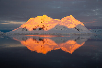 Mountain with red orange top light up by midnight sun with reflection in the sea in Antarctica 