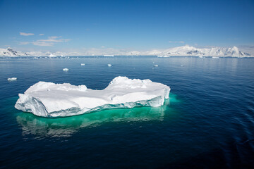 Floating iceberg with clear visible part under the water, glacier in the background and blue sky