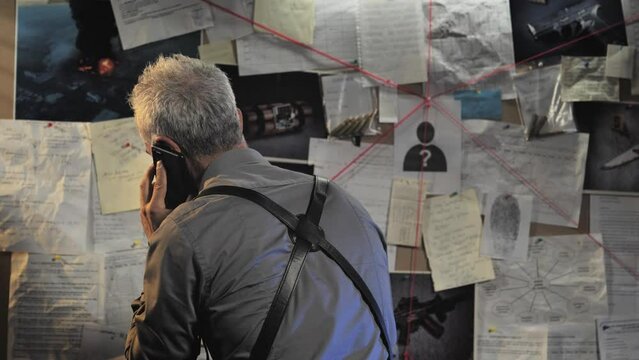 police detective male standing at the evidence board calling at the phone,policeman officer working on the murder case,crime investigation concept
