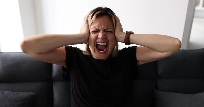 Young woman arguing and screaming angrily reacting to depression. Hysterical angry young woman broken on sofa