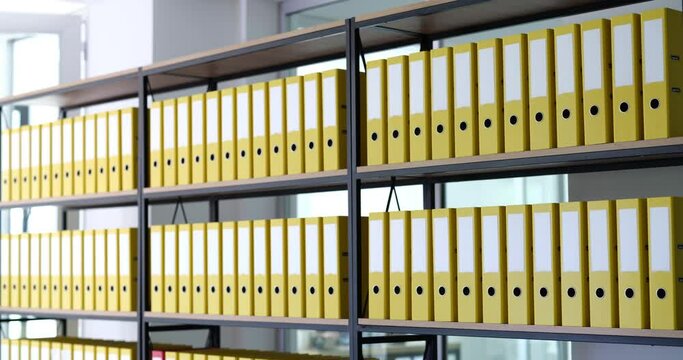 Red folder moves on shelves in row of identical yellow ones in archive. Storage of business documents