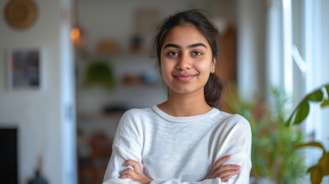 Head shot portrait smart confident smiling millennial indian woman standing with folded arms at home.
