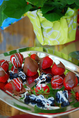 Erdbeeren und Heidelbeeren, überzogen mit Zuckerguss und Schokoglasur, auf einer silbernen Platte.
