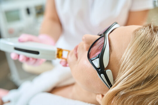 Partial image of cosmetologist doing laser epilation of woman face