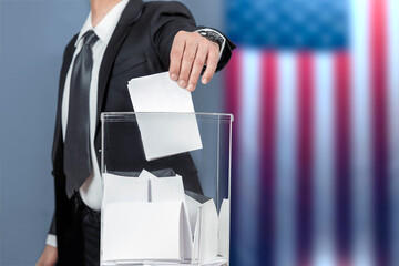 A voter casts a ballot into a ballot box on election day, USA flag