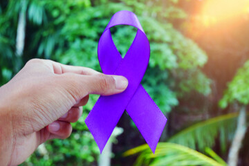 Man holding a purple ribbon as a symbol of World Cancer Day, closeup.