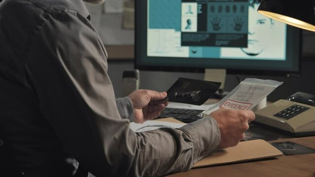 crime investigation detective examining evidence in office close up on hands,police officer sits at the desk checking photos of the murder case