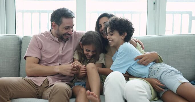 Happy middle aged Latin parents and two kids looking at camera with toothy smiles, starting tickling each other, screaming, laughing, enjoying family leisure, activity, entertainment, having fun