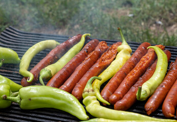Green peppers and pork sausages on the barbecue grill. Fresh anaheim chili peppers roasting over a charcoal fire. Cooking peppers at the barbecue. Cayenne pepper.