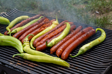 Green peppers and pork sausages on the barbecue grill. Fresh anaheim chili peppers roasting over a charcoal fire. Cooking peppers at the barbecue. Cayenne pepper.