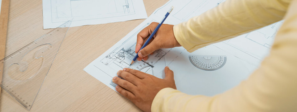 Cropped image of skilled architect designer hand draws blueprint with architectural equipment and blueprint. Creative working and design concept. Closeup. Focus on hand. Back view. Variegated.