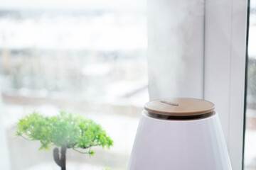 Air humidifier near the window, releasing steam, combating winter dryness, home comfort