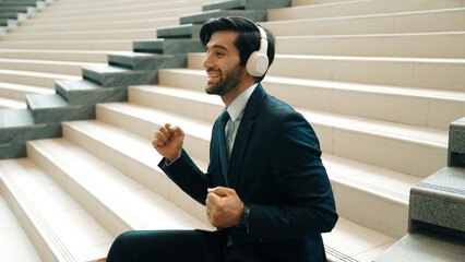 Project manager listening and enjoy music from headphone while sitting at stairs. Professional...