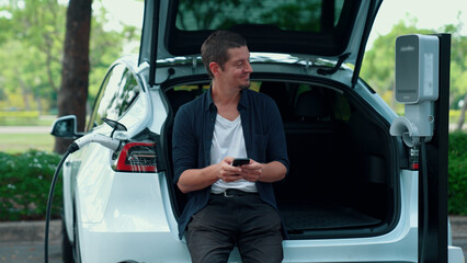 Man using smartphone online banking application to pay for electric car battery charging from EV...