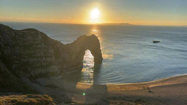 The sun goes down on the Jurassic coast and Durdle Door in Dorset with Seak Pink Trift growing on the top of the cliff in the foreground. Durdle Door, Dorset, Jurassic Coast, England, UK