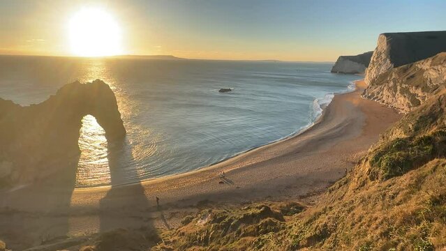 The sun goes down on the Jurassic coast and Durdle Door in Dorset with Seak Pink Trift growing on the top of the cliff in the foreground. Durdle Door, Dorset, Jurassic Coast, England, UK
