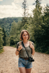 Smiling young female traveler with backpack walking by the mountain footpath