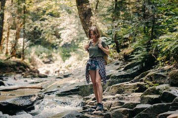 Full length of young female traveler with backpack walking by the stones along the mountain river