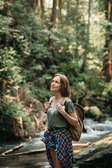 Smiling young female traveler with backpack standing by the mountain river and enjoying views