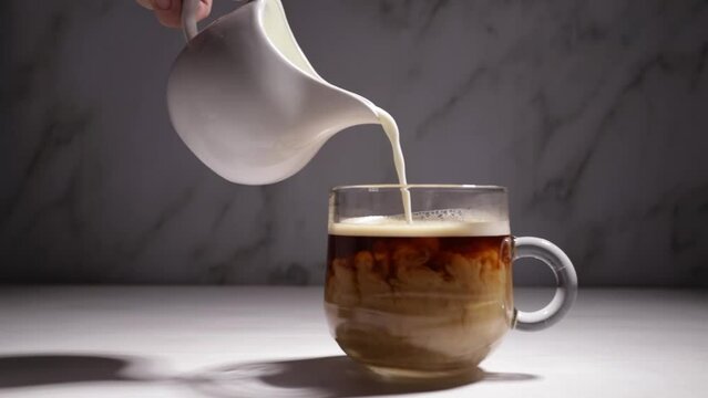 milk in coffee is poured by hand from a milk jug into a transparent cup, cream is mixed with a hot drink, Americano with milk is prepared in a cafe bar