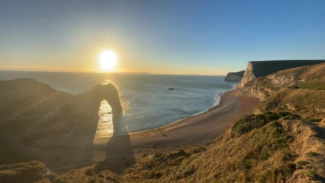 The sun goes down on the Jurassic coast and Durdle Door in Dorset with Seak Pink Trift growing on the top of the cliff in the foreground. Durdle Door, Dorset, Jurassic Coast, England, UK