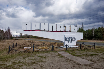The sign stands under a cloudy sky, with dry grass and bare trees around. Text in cyrillic:...