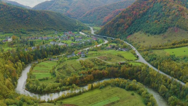 drone flies over a mountain village of houses, vegetable gardens, roads of Ukraine in the Carpathians with a picturesque forest and fog from river valleys. Golden autumn painted red
  yellow orange