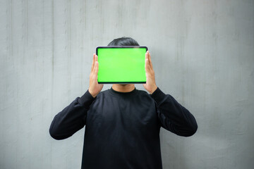 Young Asian man with a black sweater holding and pointing at an iPad tablet green screen mockup