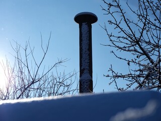 An old metal chimney on a snow-covered roof against blue sky background after snowfall.