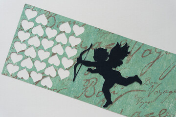 paper with multiple heart shape cutouts and a silhouette figure of a cupid holding a bow and arrow