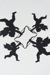 four black paper silhouettes of machine-cut winged figures (Cupids) with bows and arrows arranged...