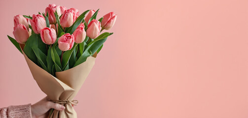 Woman hands holding a bouquet of tulips in kraft paper on a light pink background.