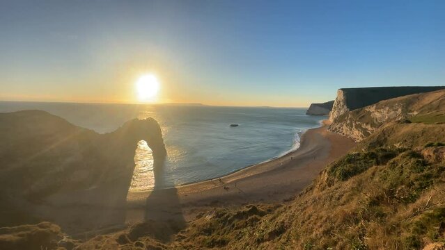 The sun goes down on the Jurassic coast and Durdle Door in Dorset with Seak Pink Trift growing on the top of the cliff in the foreground. Durdle Door, Dorset, Jurassic Coast, England, UK