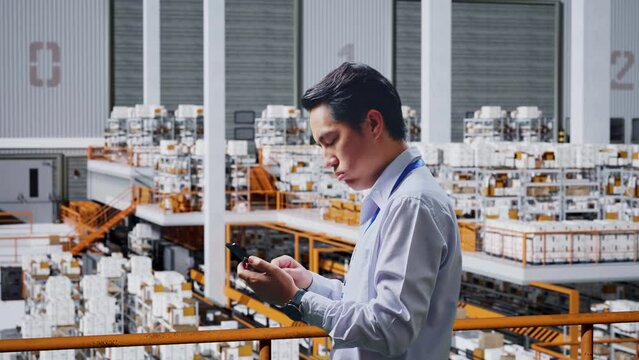 Side View Of Asian Business Man Not Satisfied And Shakes His Head While Using Mobile Phone In The Warehouse
