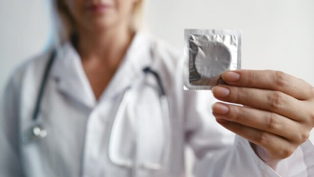 Doctor showing condom at camera, importance of contraception and sex education - Powered by Adobe
