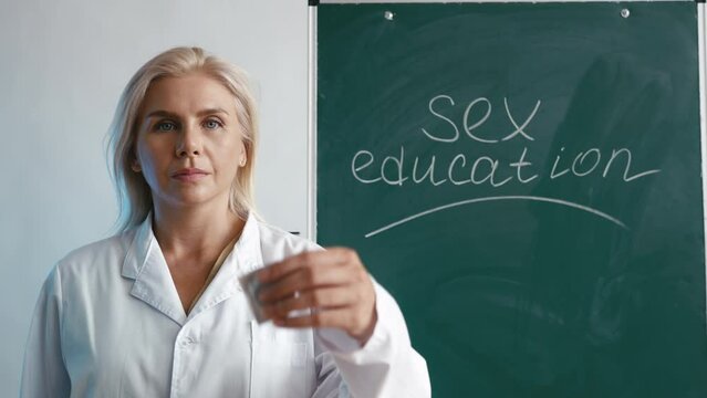 Sex education teacher demonstrating a condom to students near a chalkboard