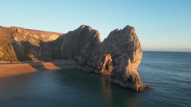 The sun goes down on the Jurassic coast and Durdle Door in Dorset with Seak Pink Trift growing on the top of the cliff in the foreground. Durdle Door, Dorset, Jurassic Coast, England, UK
