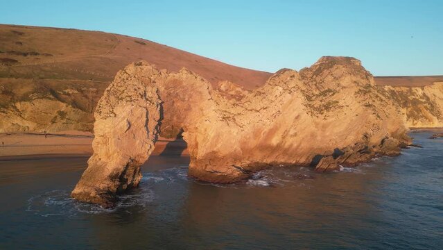 The sun goes down on the Jurassic coast and Durdle Door in Dorset with Seak Pink Trift growing on the top of the cliff in the foreground. Durdle Door, Dorset, Jurassic Coast, England, UK