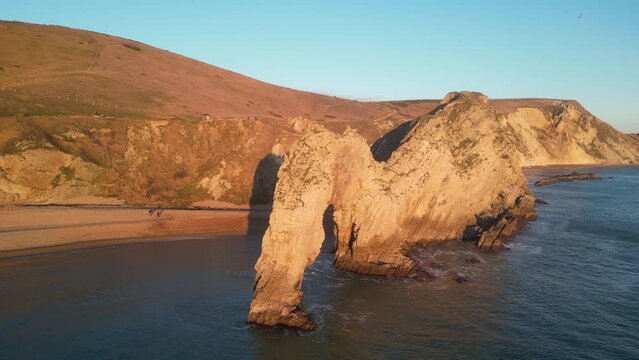 The sun goes down on the Jurassic coast and Durdle Door in Dorset with Seak Pink Trift growing on the top of the cliff in the foreground. Durdle Door, Dorset, Jurassic Coast, England, UK