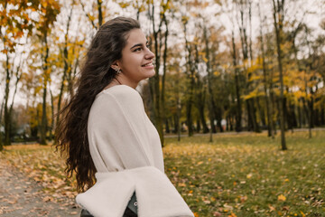 Attractive pretty woman walking outdoor, portrait of young lady in warm sunny autumn park season, fall, yellow orange red leaves, dressed leather wool fur jacket smiling having fun 

