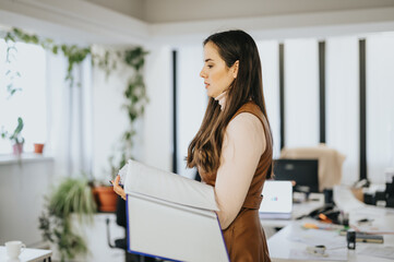 Focused businesswoman carrying a box of belongings in an office, depicting change, relocation or...
